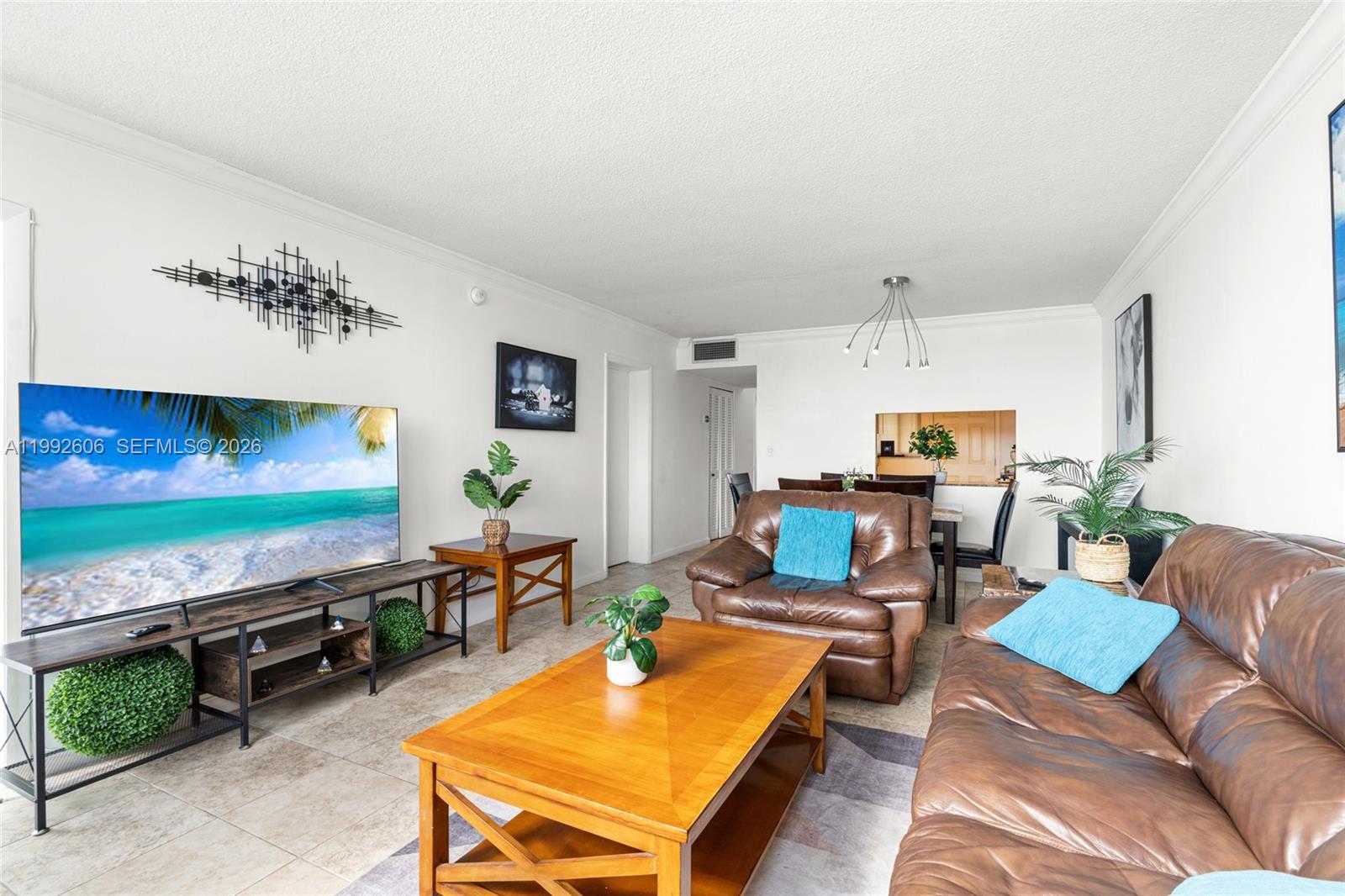 A living room features a large television, brown leather furniture, and tile flooring — 1170 NE 191st St # 35, Miami FL 33179, MIAMI, FL