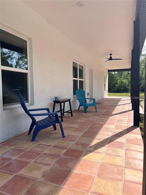 A covered patio features terracotta-colored square tiles, a ceiling fan, and two blue plastic chairs — 456 BARON ROAD, ORLANDO, FL