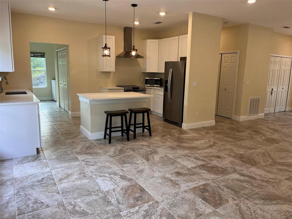 A kitchen features white cabinets, a central island with two stools, and tile flooring — 456 BARON ROAD, ORLANDO, FL