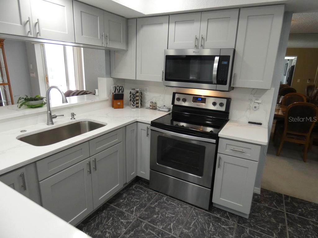A kitchen features gray cabinets, stainless steel appliances, and white countertops with dark tiled floors — 8158 WINDING OAK LANE, SPRING HILL, FL