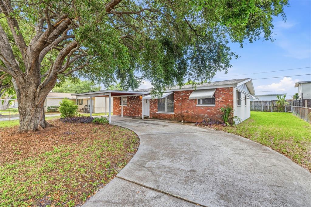 A single-story brick house features a concrete driveway, a carport, and a large oak tree — 4408 W ELM STREET, TAMPA, FL