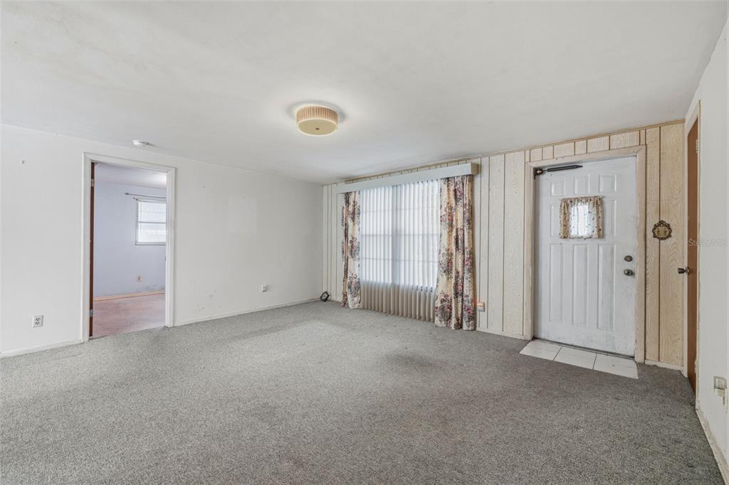 An empty living room features gray carpeting, white walls, wood paneling, and a front door — 4408 W ELM STREET, TAMPA, FL