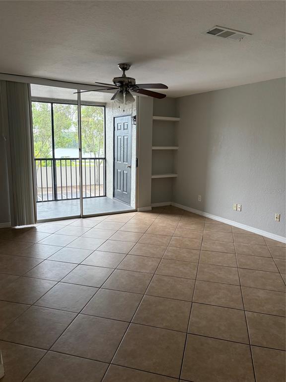 An empty living room features tile flooring, a ceiling fan, built-in shelves, and a balcony — 7511 SEURAT STREET UNIT 10201, ORLANDO, FL