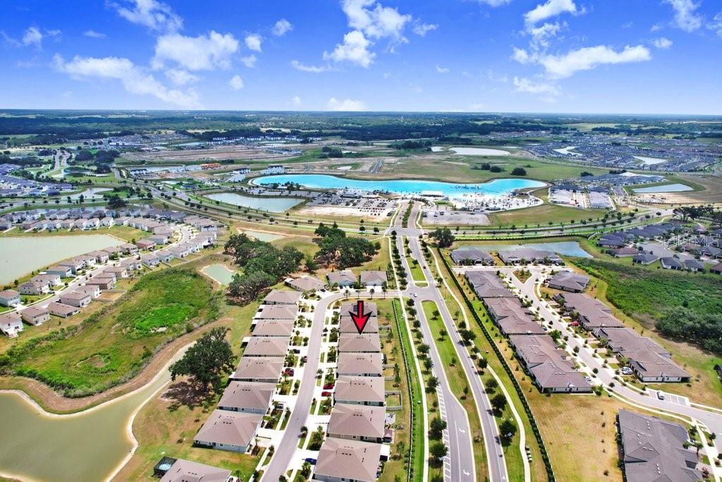 An aerial view shows a suburban neighborhood with townhomes, a large lagoon, and surrounding landscape — 31426 MANGO FADE WAY, SAN ANTONIO, FL