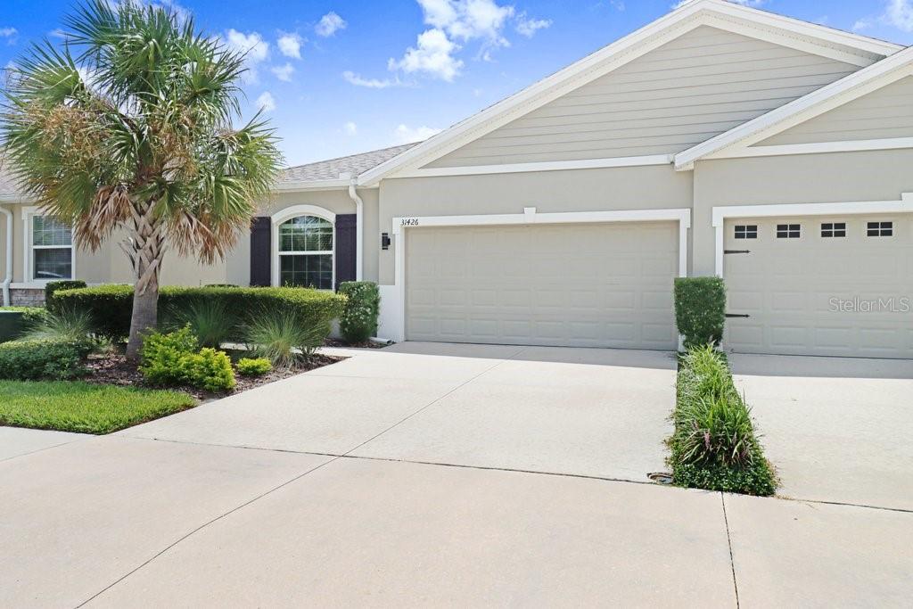A beige house exterior features a two-car garage, a palm tree, and a concrete driveway — 31426 MANGO FADE WAY, SAN ANTONIO, FL