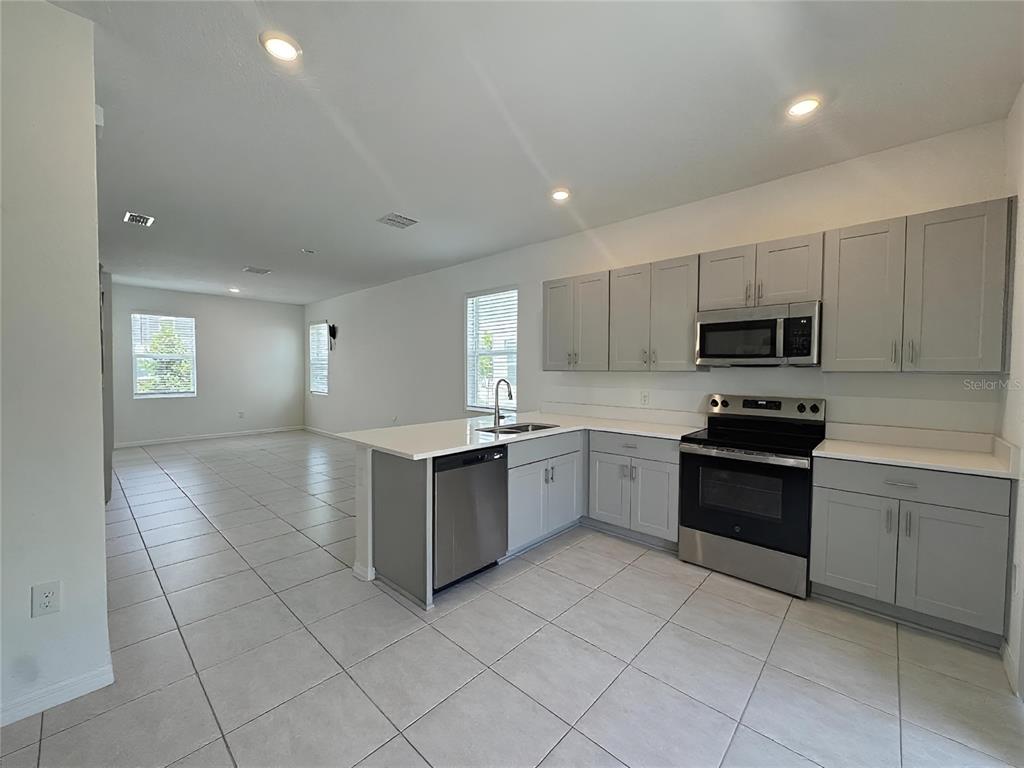 A kitchen with gray cabinets and stainless steel appliances opens to a tiled living area — 3093 SKYLINE LOOP, KISSIMMEE, FL