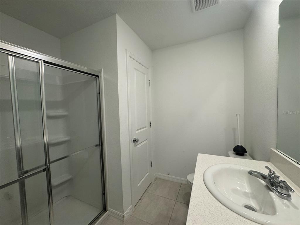A bathroom features a glass-enclosed shower, a white vanity with a sink, and tile flooring — 3093 SKYLINE LOOP, KISSIMMEE, FL