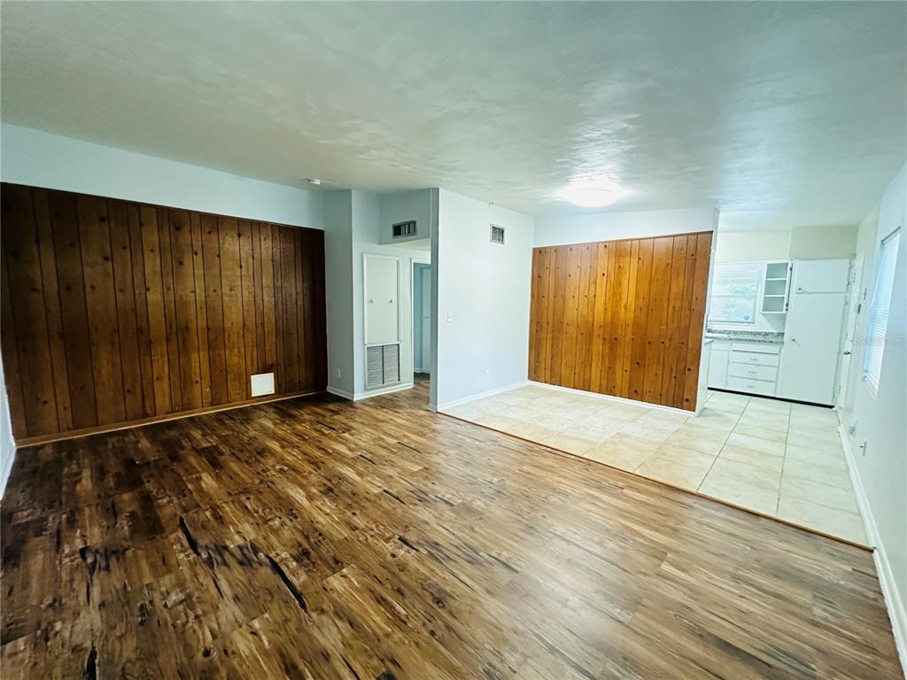 An open-concept living room and kitchen area featuring wood-paneled accent walls and mixed flooring — 6033 BALBOA DRIVE, ORLANDO, FL