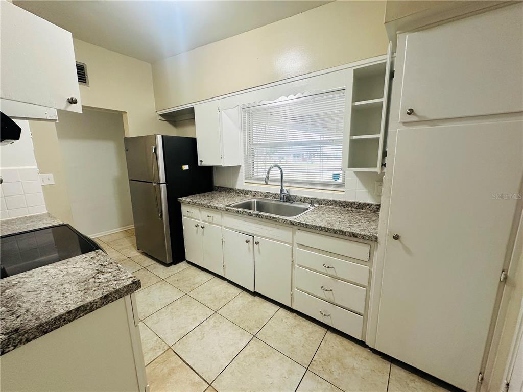 A kitchen features white cabinets, granite countertops, a stainless steel refrigerator, and tiled flooring — 6033 BALBOA DRIVE, ORLANDO, FL