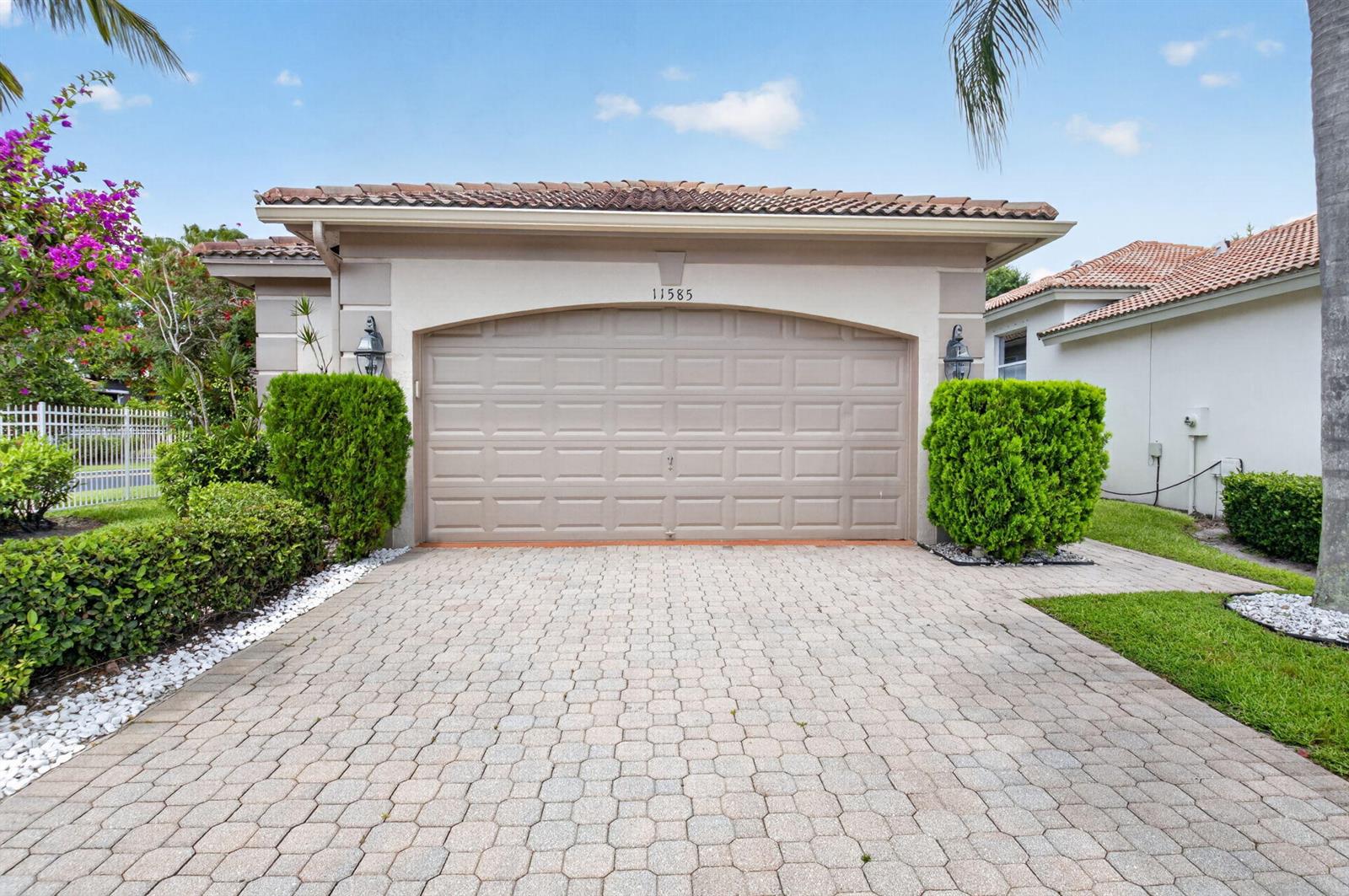 A beige house exterior features a two-car garage, a paved driveway, and manicured landscaping — 11585 Green Golf Lane, Boynton Beach FL 33437, BOYNTON BEACH, FL
