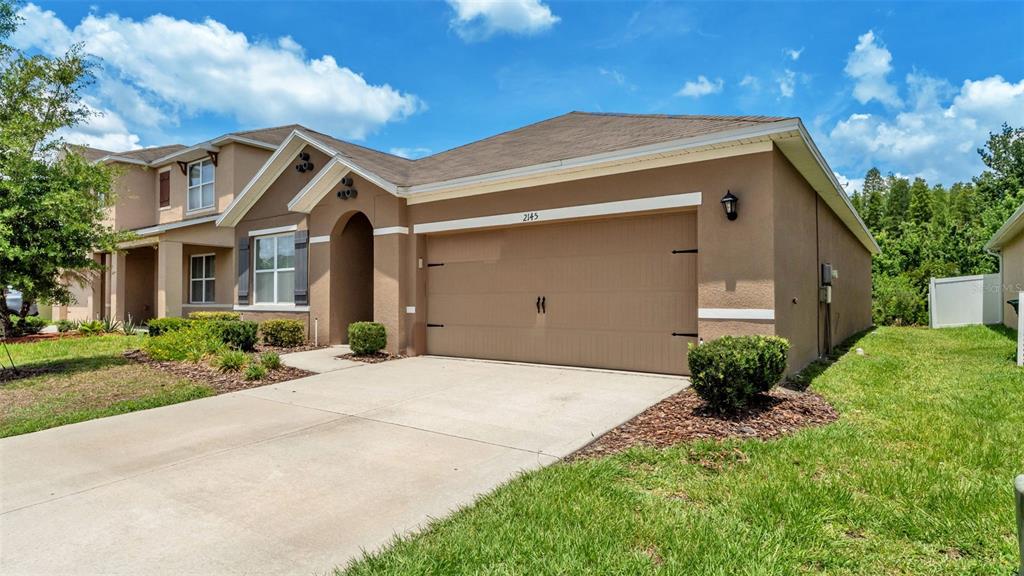 A tan, two-story suburban house features a two-car garage and a concrete driveway — 2145 BLUE HIGHLANDS DRIVE, LAKELAND, FL
