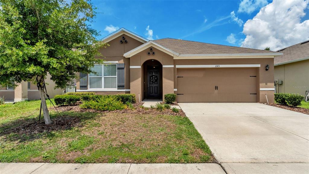 A single-story tan house with a two-car garage and a front yard with a tree — 2145 BLUE HIGHLANDS DRIVE, LAKELAND, FL