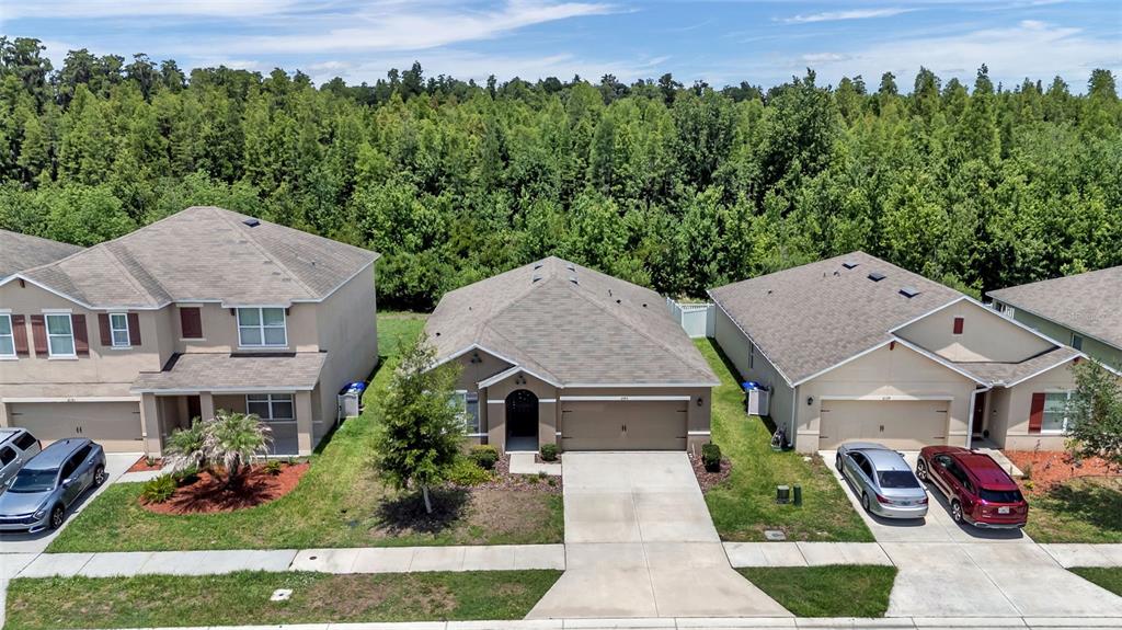 An aerial view shows three suburban houses with driveways and garages bordering a dense forest — 2145 BLUE HIGHLANDS DRIVE, LAKELAND, FL