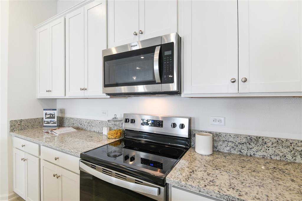 A kitchen features white cabinets, granite countertops, and stainless steel appliances including a microwave and stove — 3445 GOLDEN EYE DRIVE, ORANGE PARK, FL