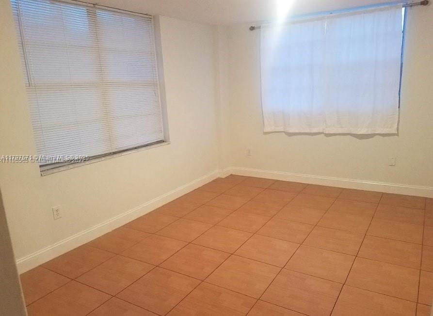 An empty room features white walls, tiled flooring, and two windows with blinds and curtains — 15600 NW 7th Ave # 319, Miami FL 33169, MIAMI, FL