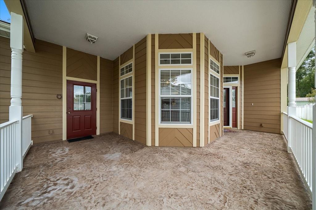 A covered porch with brown siding, a textured concrete floor, and two red entry doors — 4014 NE 23RD PLACE, OCALA, FL