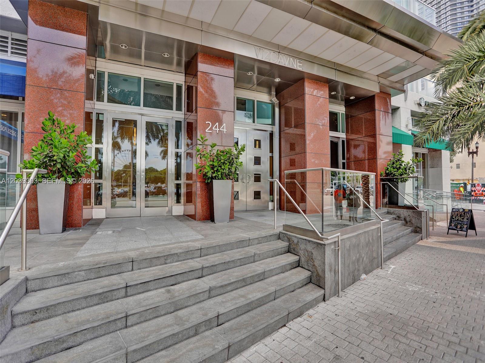The exterior entrance of a building features red stone columns, glass doors, and concrete steps — 244 Biscayne Blvd # 3409, Miami FL 33132, MIAMI, FL