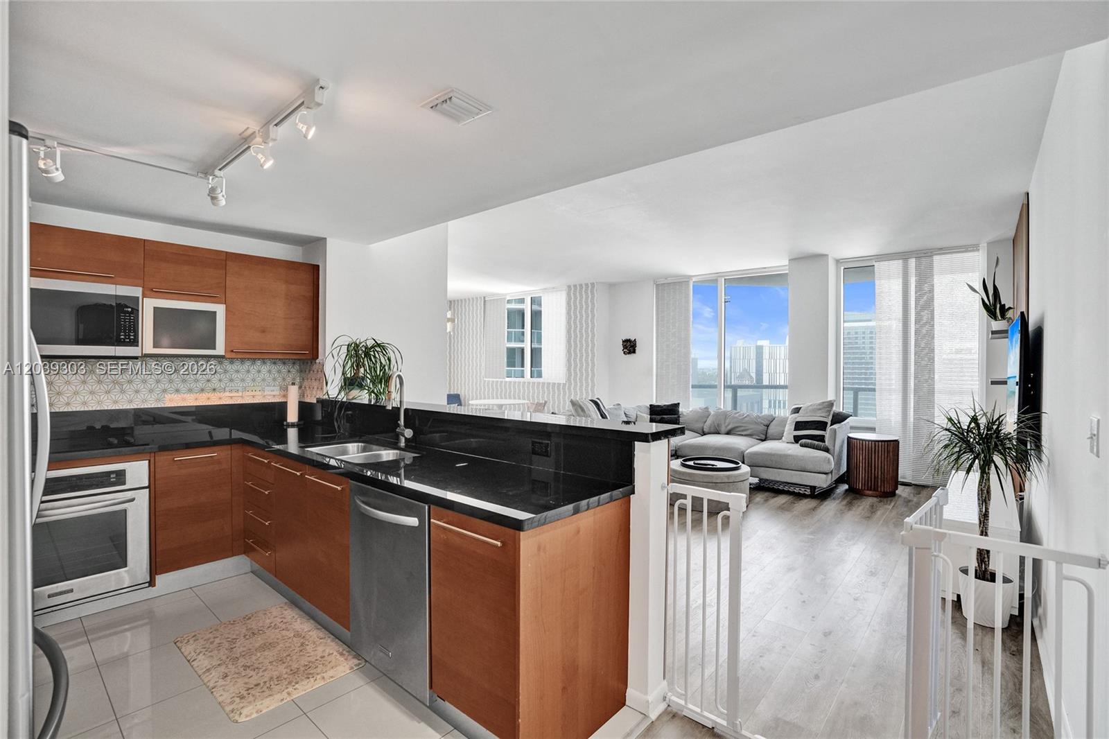 A kitchen with wood cabinets and black countertops opens into a living room with views — 244 Biscayne Blvd # 3409, Miami FL 33132, MIAMI, FL