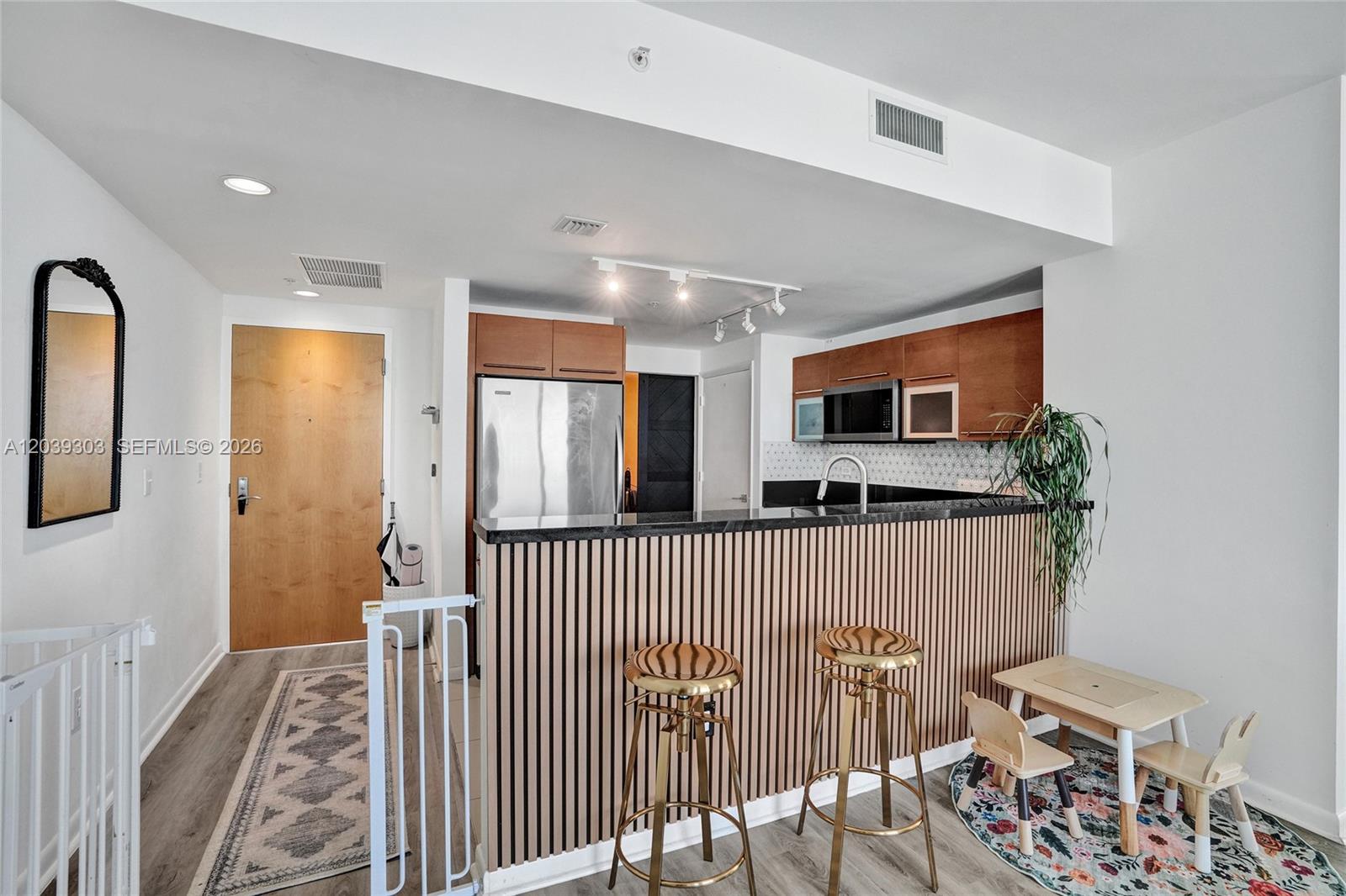 A kitchen features wood-slat cabinetry, stainless steel appliances, and a breakfast bar with gold stools — 244 Biscayne Blvd # 3409, Miami FL 33132, MIAMI, FL