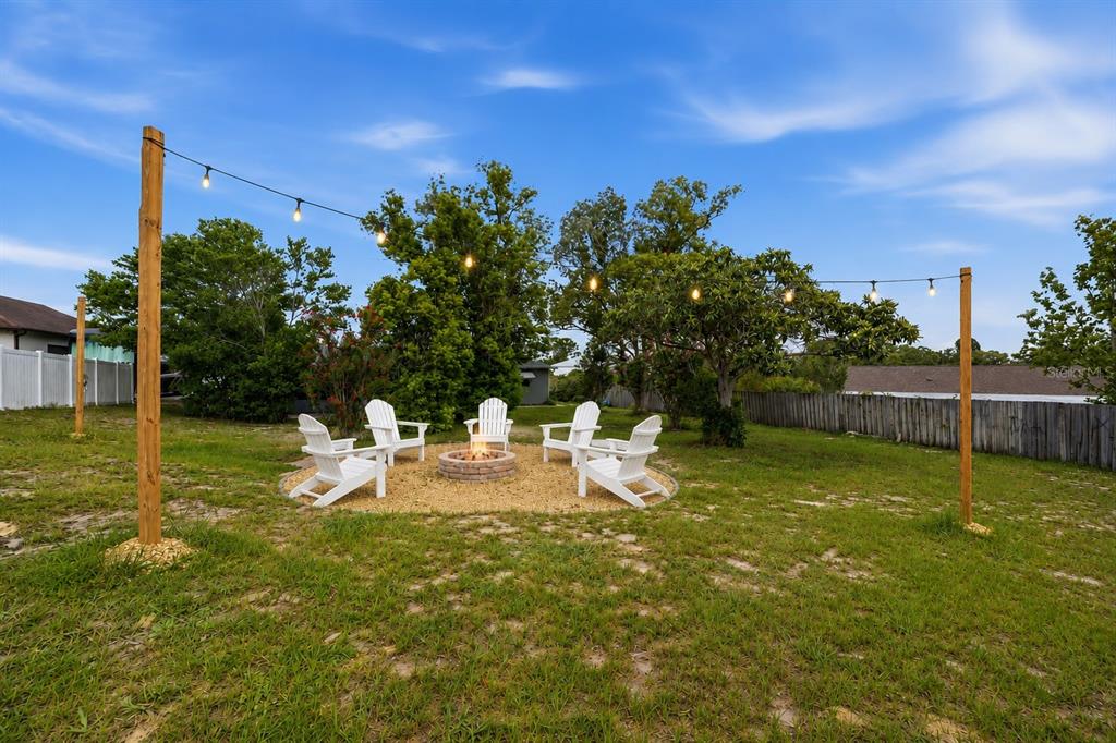 A backyard features a circular gravel fire pit area with white chairs and string lights — 6310 GAINSBORO AVENUE, SPRING HILL, FL