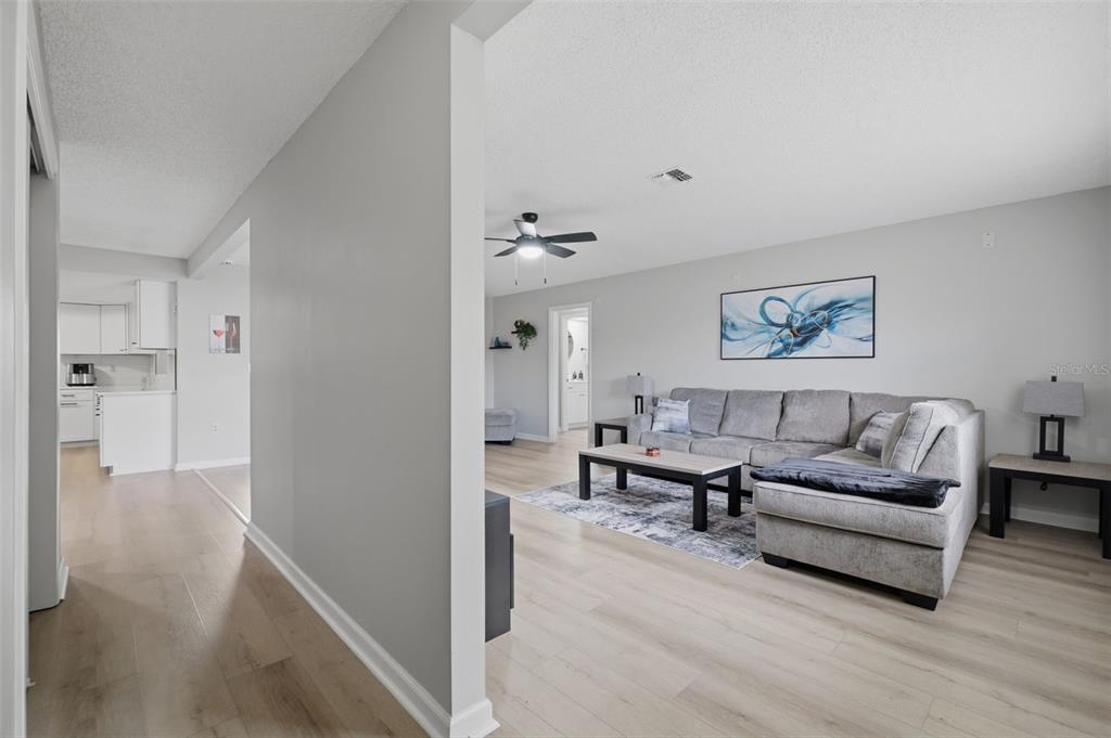 A living room with light wood flooring, a gray sectional sofa, and an adjacent kitchen — 6310 GAINSBORO AVENUE, SPRING HILL, FL