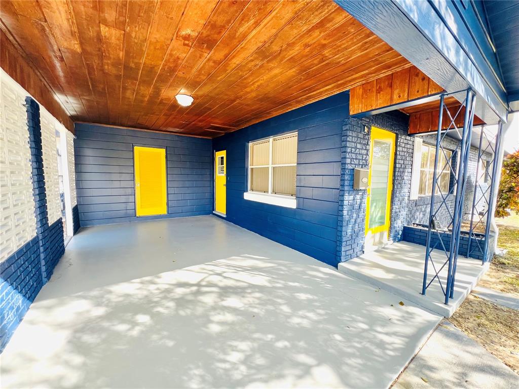 A covered porch with a wood-paneled ceiling, blue brick walls, and bright yellow doors — 501 AVENUE G SE UNIT A, WINTER HAVEN, FL