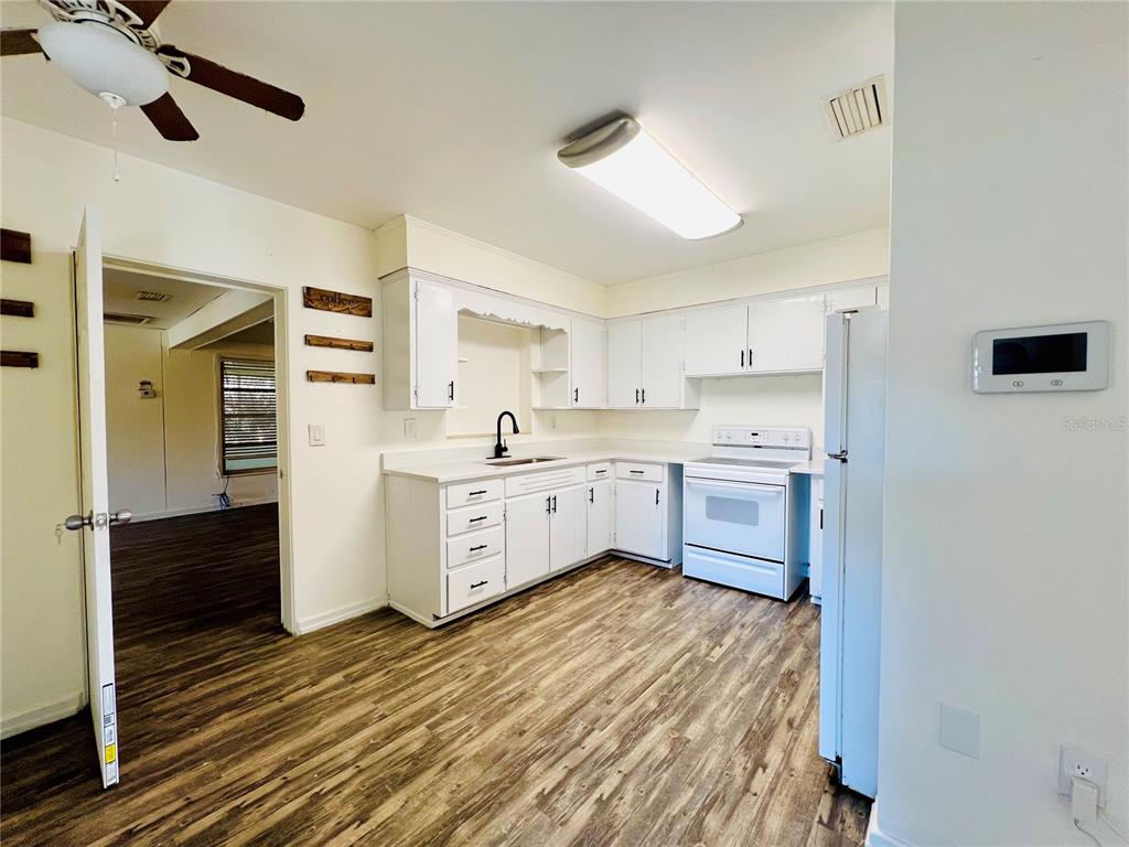 A kitchen with white cabinets, white appliances, and wood-look flooring — 501 AVENUE G SE UNIT A, WINTER HAVEN, FL