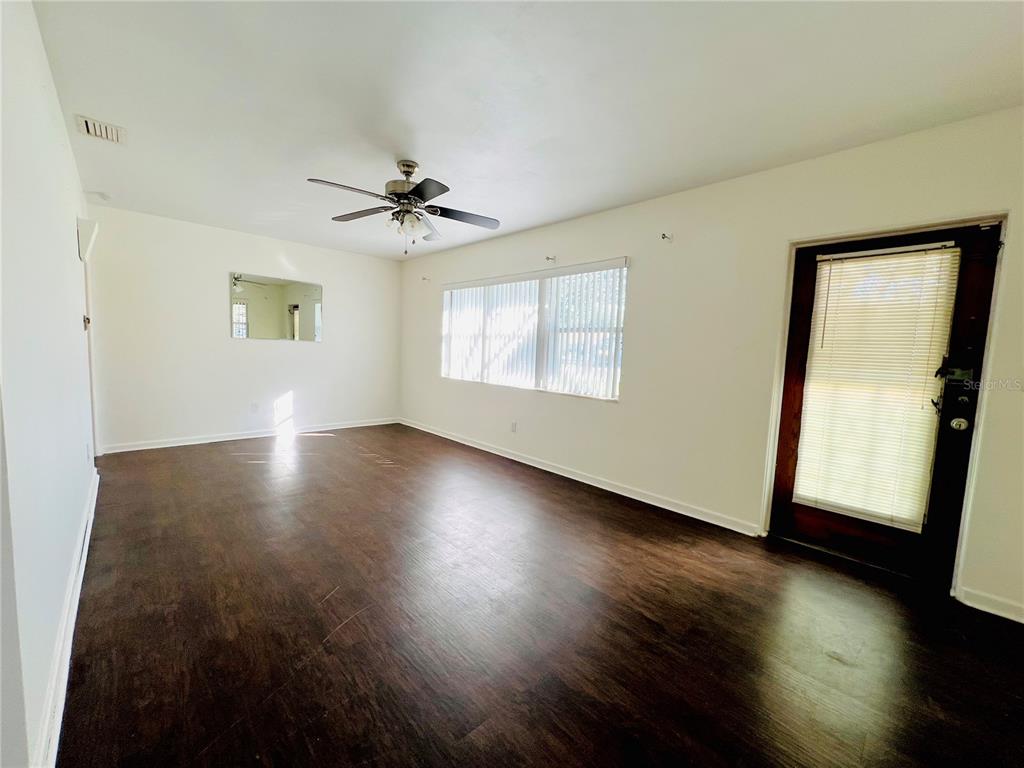A living room features dark wood-look flooring, white walls, a ceiling fan, and a glass door — 501 AVENUE G SE UNIT A, WINTER HAVEN, FL