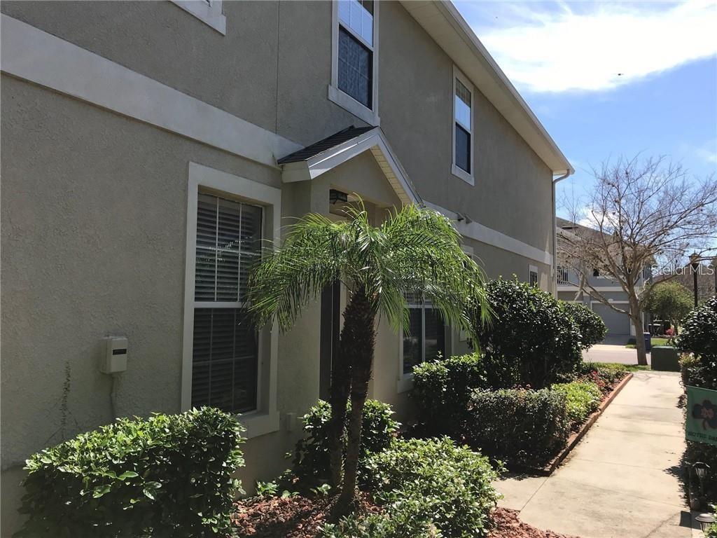 A beige two-story townhouse features a small palm tree and landscaping near the front entrance — 7542 RED MILL CIRCLE, NEW PORT RICHEY, FL