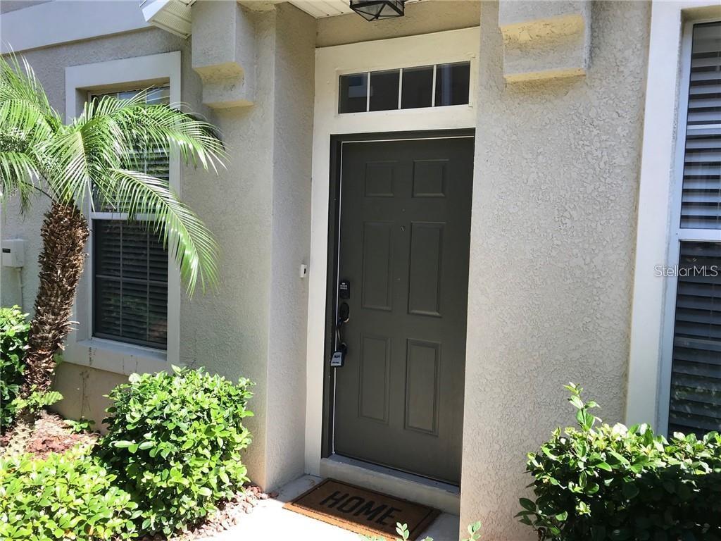 A dark gray front door with a transom window sits between two windows and landscaping — 7542 RED MILL CIRCLE, NEW PORT RICHEY, FL