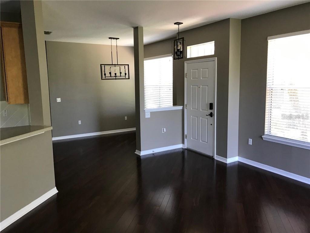 An open-concept living area features dark hardwood floors, neutral walls, and a dining room chandelier — 7542 RED MILL CIRCLE, NEW PORT RICHEY, FL