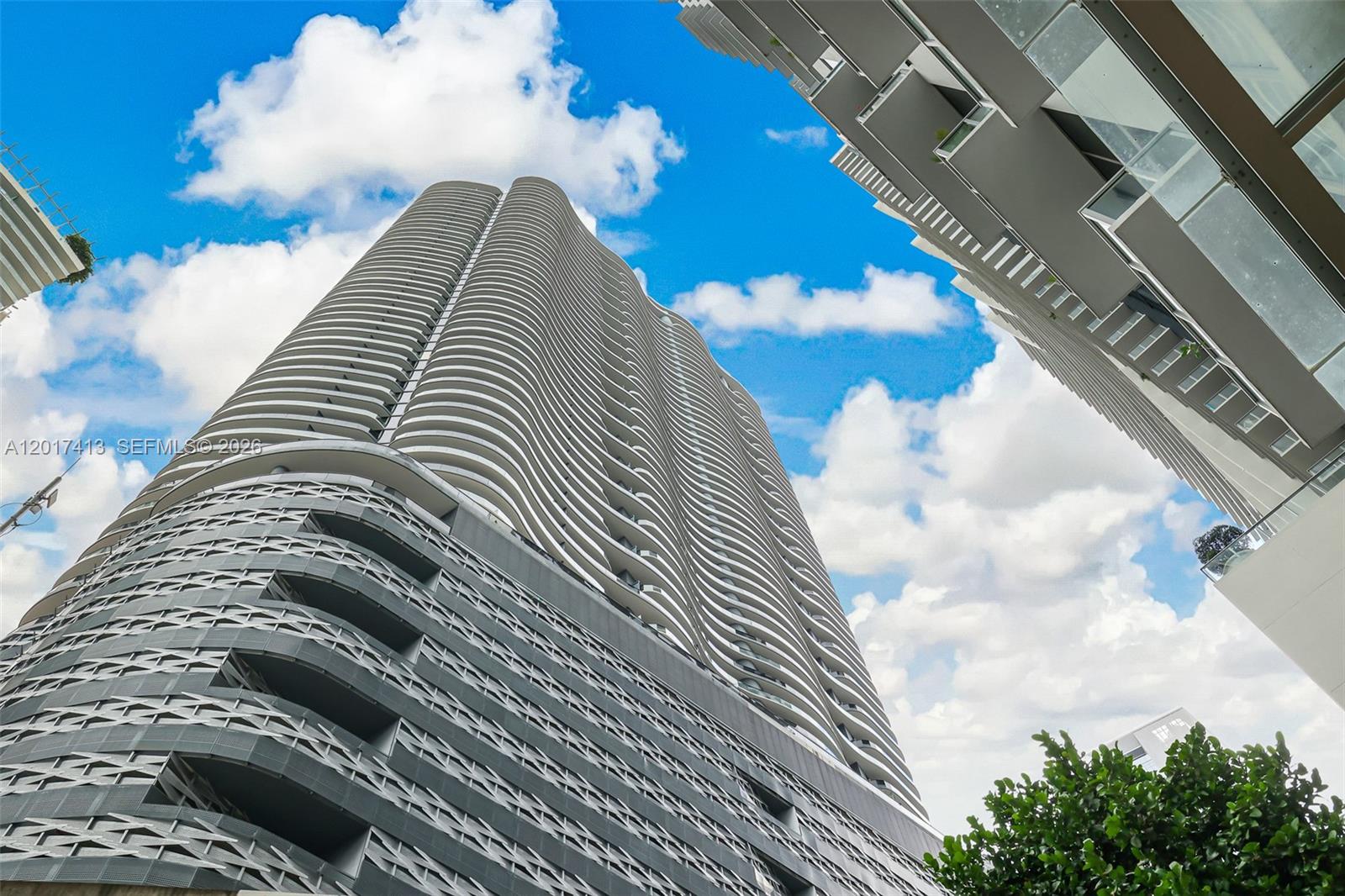 A low-angle view shows the exterior of a modern high-rise building with curved balconies — 1000 Brickell Plz # 3002, Miami FL 33131, MIAMI, FL