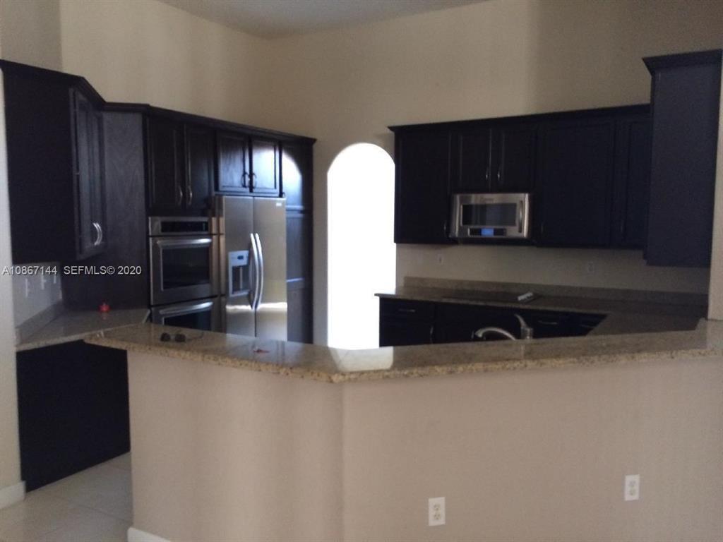 A kitchen features dark wood cabinets, stainless steel appliances, and a granite-topped breakfast bar — 19080 SW 24th Street, Miramar FL 33029, MIRAMAR, FL