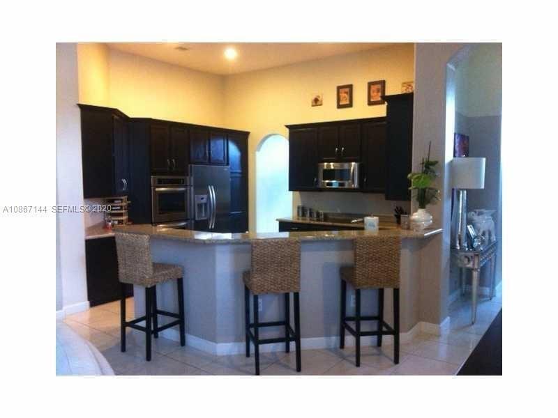 A kitchen features dark wood cabinets, granite countertops, and three wicker bar stools — 19080 SW 24th Street, Miramar FL 33029, MIRAMAR, FL