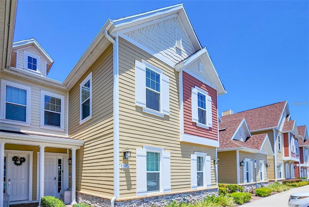 A two-story townhouse with tan siding, white shutters, and a red accent wall — 7595 SUNNY DREAMS LANE, KISSIMMEE, FL
