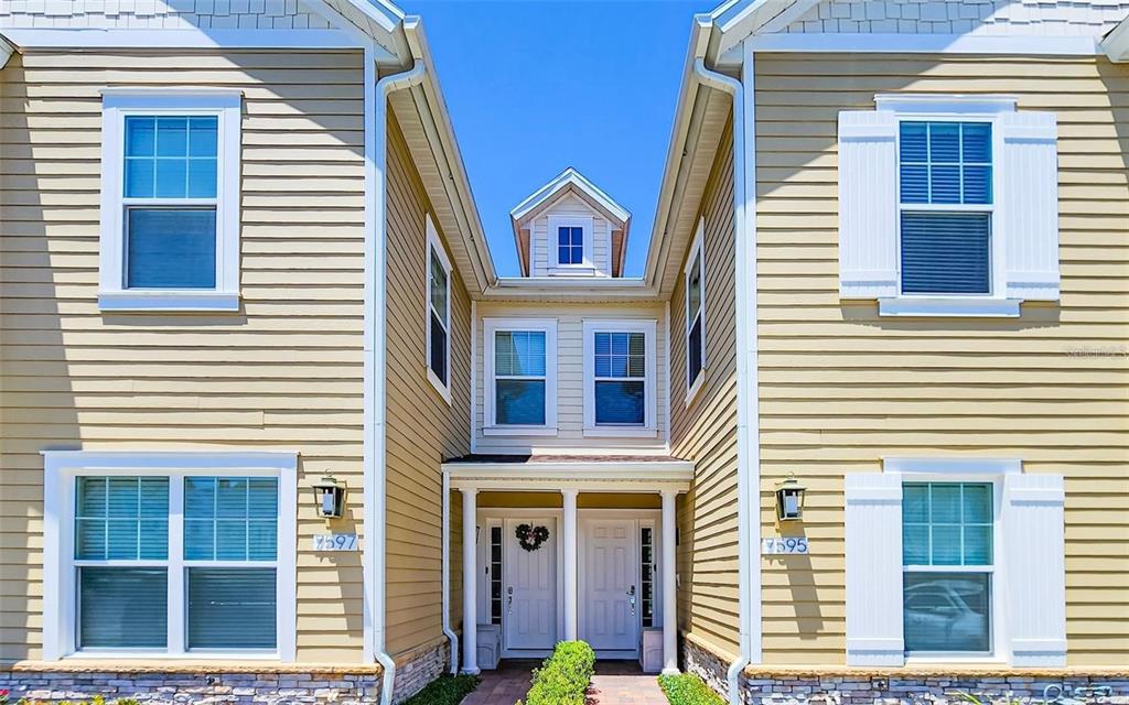 A two-story townhouse exterior with beige siding, white trim, and two adjacent front entrances — 7595 SUNNY DREAMS LANE, KISSIMMEE, FL