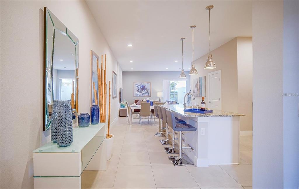 A modern kitchen with a granite island and bar stools opens into a dining area — 7595 SUNNY DREAMS LANE, KISSIMMEE, FL