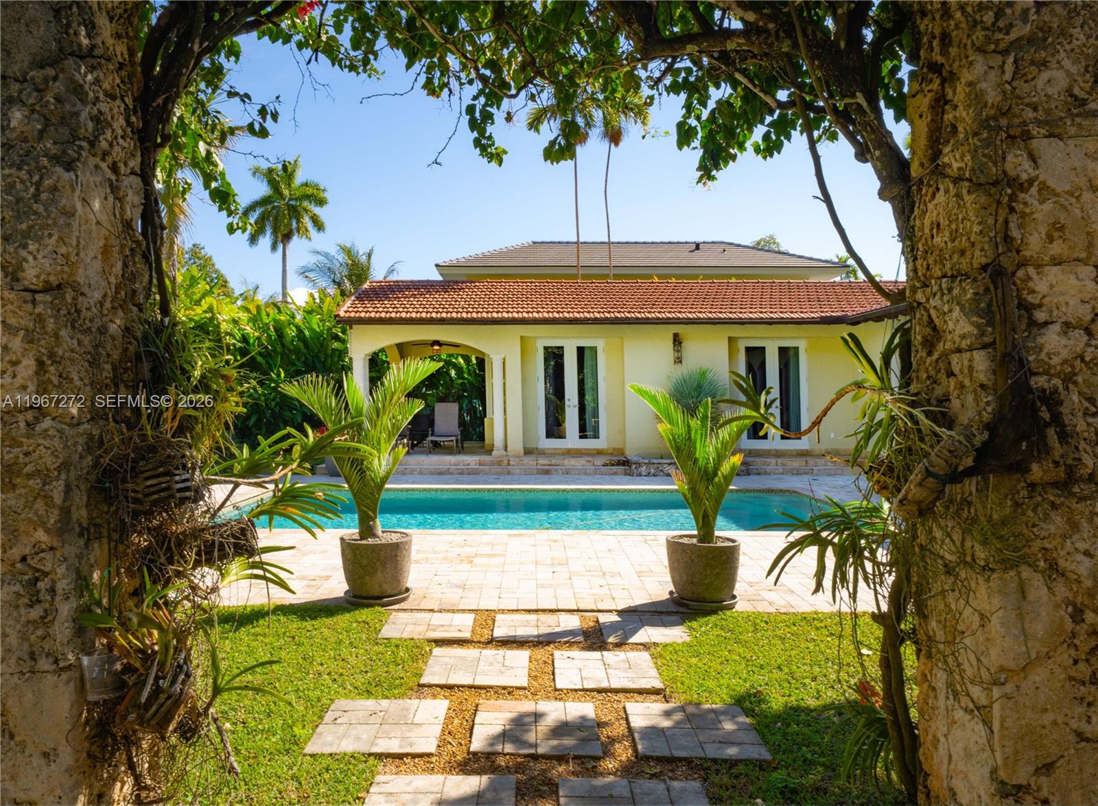 A backyard features a swimming pool, a paved patio, and a yellow house with French doors — 4867 SW 82nd St, Miami FL 33143, MIAMI, FL