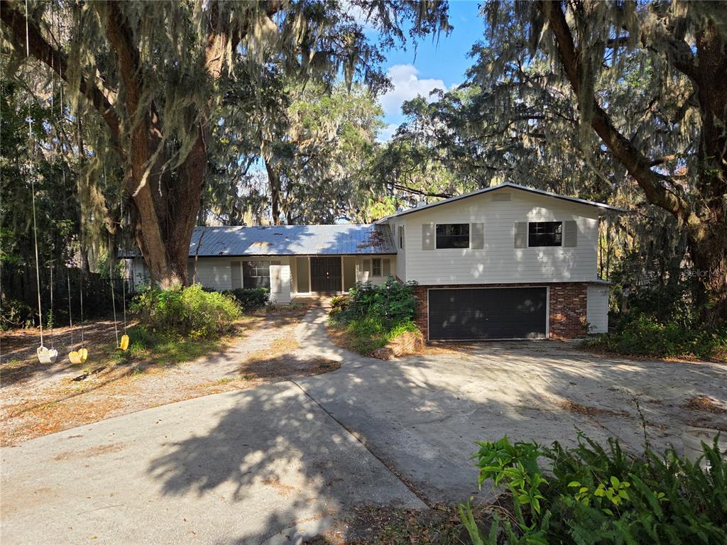 A two-story house with white siding, a metal roof, and a garage sits among trees — 2901 SW 4TH COURT, GAINESVILLE, FL