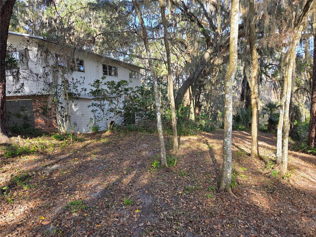 A two-story house with white siding and a brick base sits among trees — 2901 SW 4TH COURT, GAINESVILLE, FL