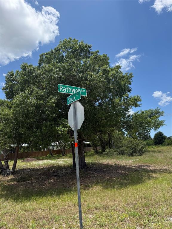 A street sign for Rathwell Avenue and Sioux Street stands in a grassy, wooded lot — 12526 RATHWELL AVENUE, PORT CHARLOTTE, FL