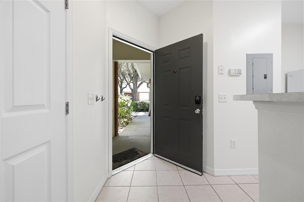 An open dark gray front door reveals a walkway and trees outside a tiled entryway — 13200 W NEWBERRY ROAD UNIT F-29, NEWBERRY, FL