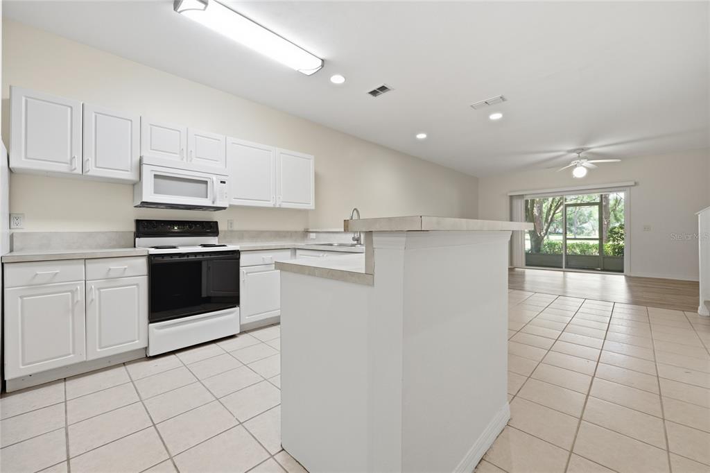 A kitchen with white cabinets, a black stove, and a tiled floor faces a living area — 13200 W NEWBERRY ROAD UNIT F-29, NEWBERRY, FL