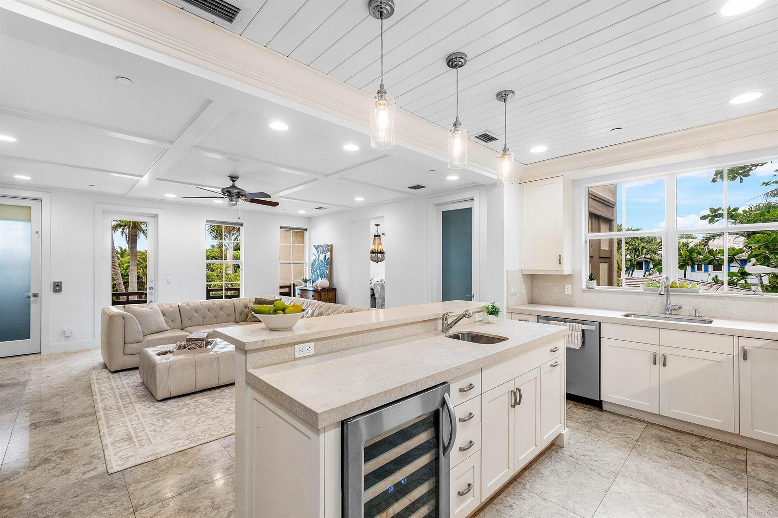 A modern kitchen with white cabinetry and a central island overlooks an open living area — 1108 Coconut Row, Delray Beach FL 33483, DELRAY BEACH, FL