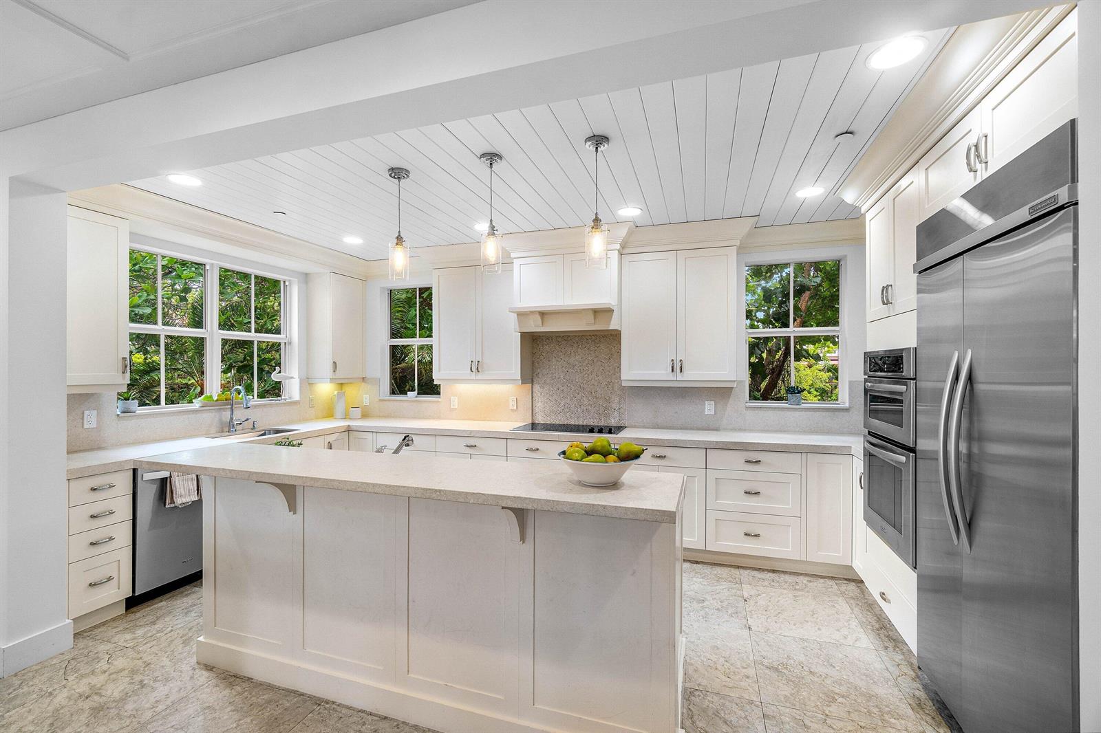 A bright kitchen features white cabinetry, a central island, stainless steel appliances, and tile flooring — 1108 Coconut Row, Delray Beach FL 33483, DELRAY BEACH, FL
