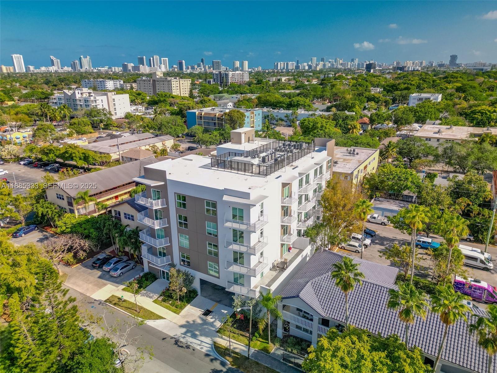 An aerial view shows a modern multi-story apartment building surrounded by trees and urban development — 1938 Jackson St # 306, Hollywood FL 33020, HOLLYWOOD, FL