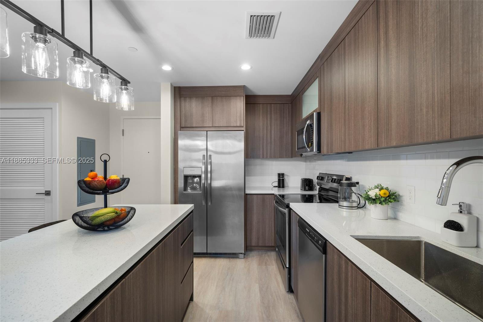A modern kitchen features wood-tone cabinetry, stainless steel appliances, and a white quartz island — 1938 Jackson St # 306, Hollywood FL 33020, HOLLYWOOD, FL
