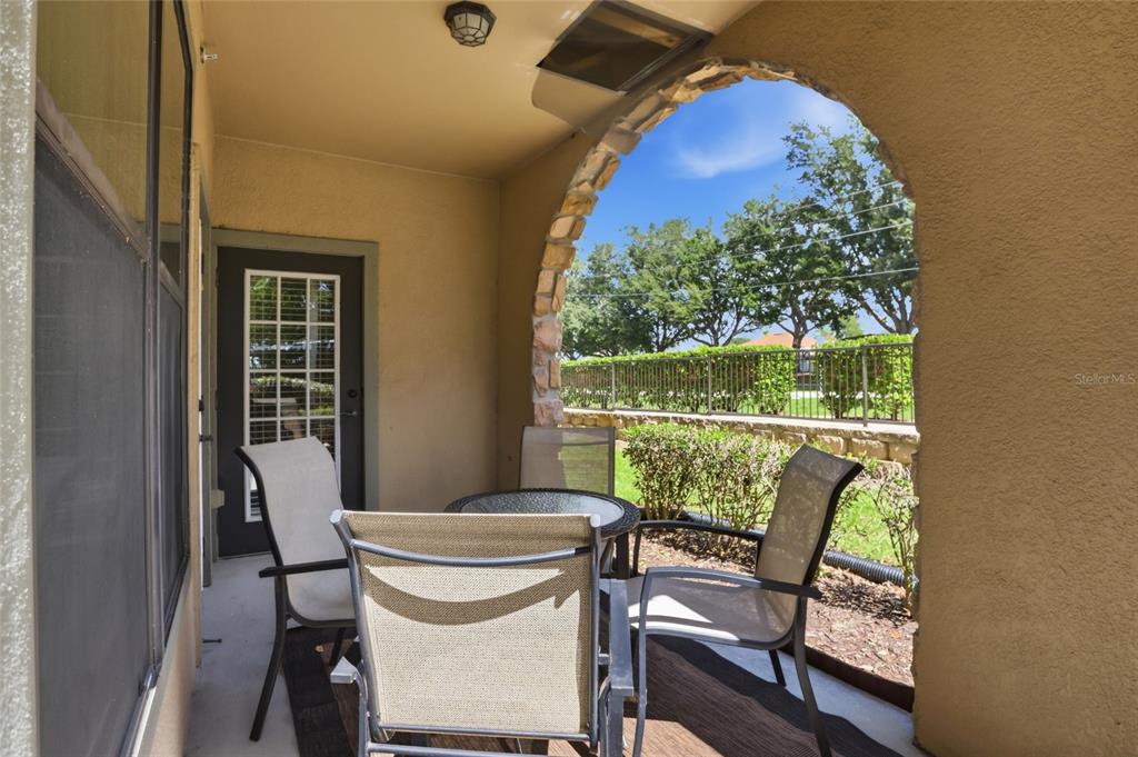 A covered patio features a stone-arched opening, outdoor furniture, and a view of the yard — 901 CHARO PARKWAY UNIT 717, DAVENPORT, FL