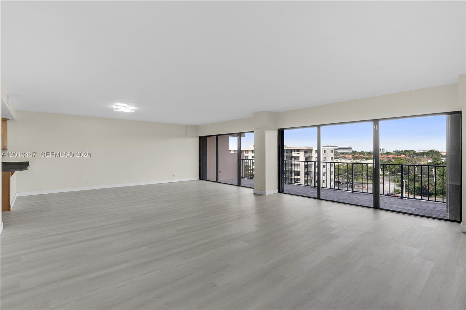 An empty living area features light wood-look flooring, neutral walls, and large sliding glass doors — 1800 NE 114th St # 601, Miami FL 33181, MIAMI, FL