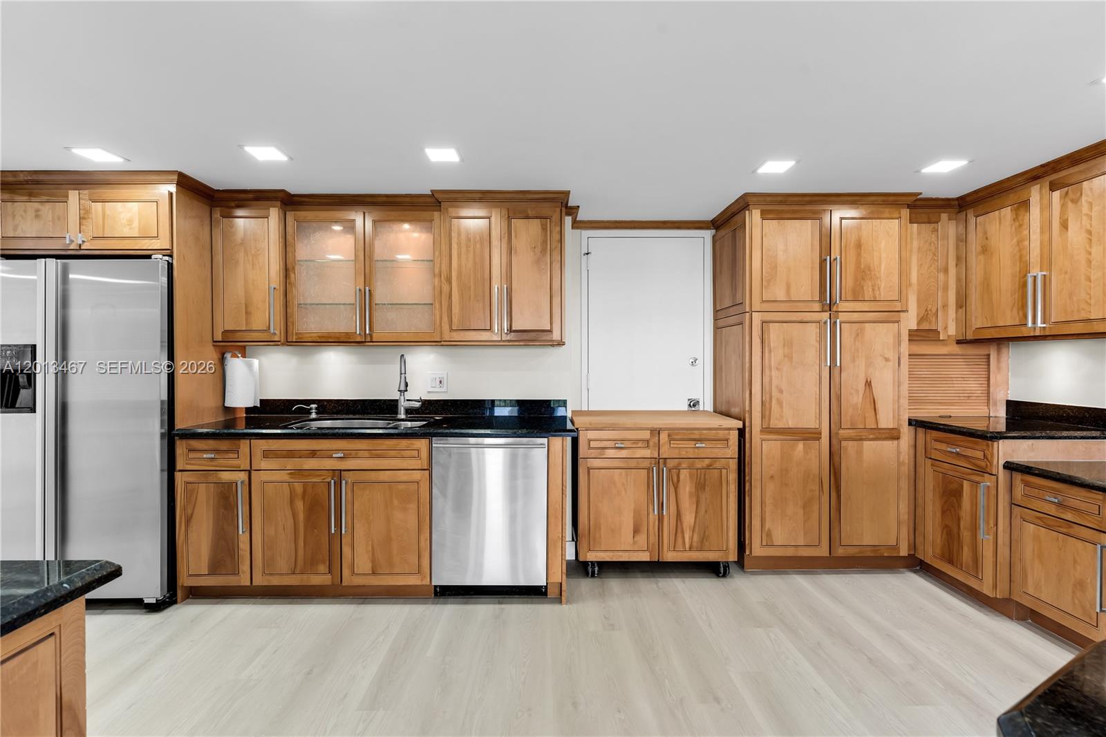 A kitchen features wood cabinets, stainless steel appliances, and black countertops on light flooring — 1800 NE 114th St # 601, Miami FL 33181, MIAMI, FL